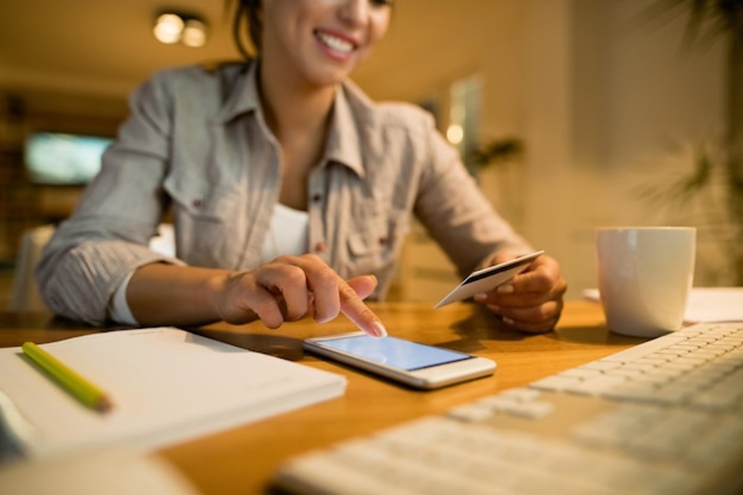 Mujer con tarjeta de crédito y smartphone mientras compra en línea en casa