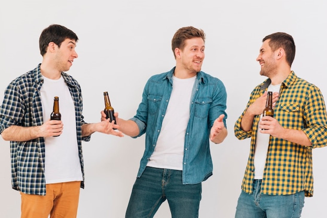 ¡Aquí entre amigos! Pero… ¿quién de ellos es el Amigo Faltón que siempre pone excusas? Si tiene a alguien en mente, esta es su oportunidad de nominarlo y hacerlo competir por un año de cerveza gratis Amigos jóvenes felices sosteniendo una botella de cerveza en la mano y burlándose