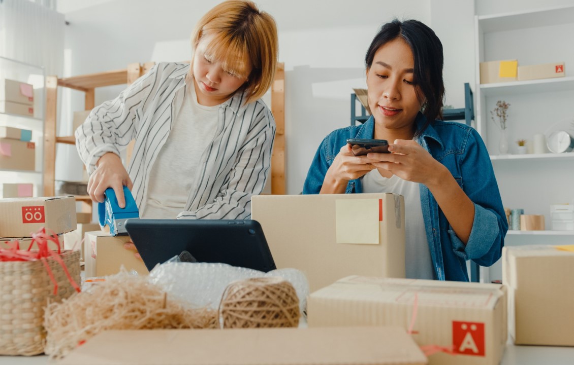 Jóvenes empresarias asiáticas que usan un teléfono móvil para recibir una orden de compra y verificar el producto en el trabajo de stock en la oficina en casa